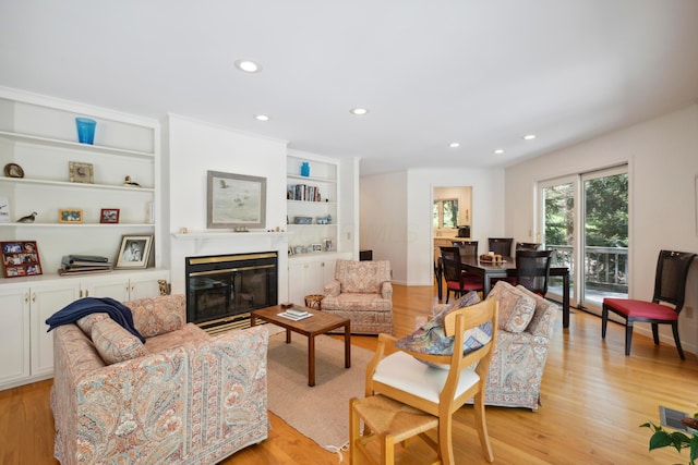 living room featuring a glass covered fireplace, built in features, light wood-style floors, and recessed lighting