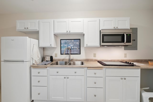 kitchen featuring a sink, black electric cooktop, freestanding refrigerator, white cabinetry, and stainless steel microwave