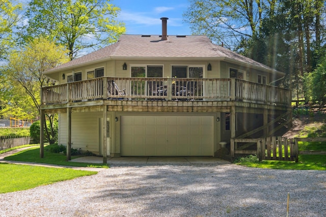 back of house featuring driveway, roof with shingles, a deck, fence, and an attached garage