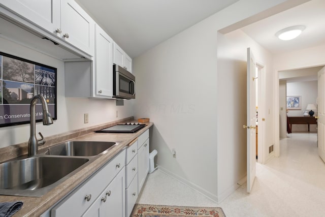 kitchen with a sink, baseboards, light countertops, stainless steel microwave, and white cabinetry