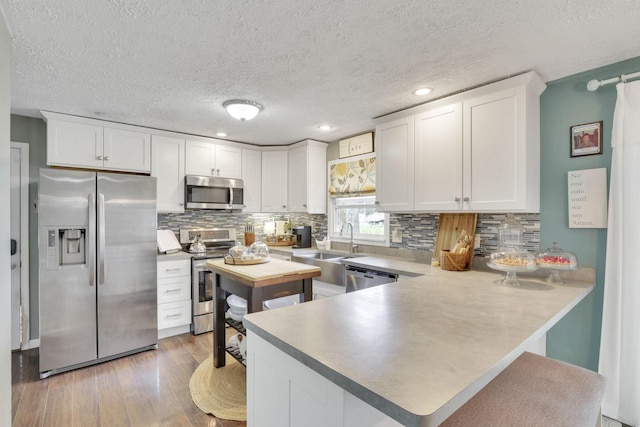 kitchen featuring white cabinets, a textured ceiling, stainless steel appliances, a peninsula, and wood finished floors