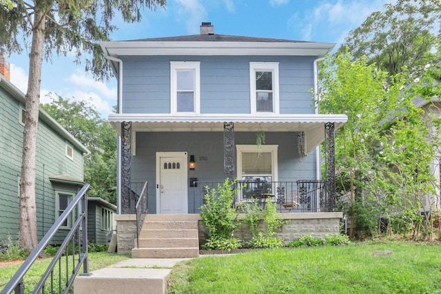 american foursquare style home featuring a front lawn, covered porch, and a chimney
