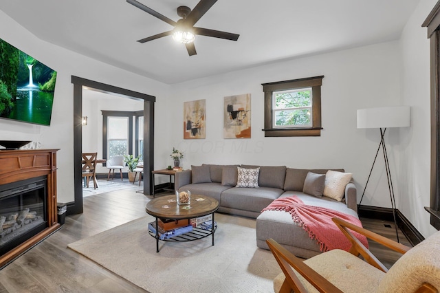 living room with a glass covered fireplace, plenty of natural light, ceiling fan, and wood finished floors