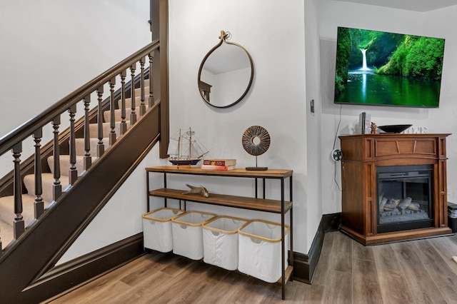 staircase with baseboards, a glass covered fireplace, and wood finished floors
