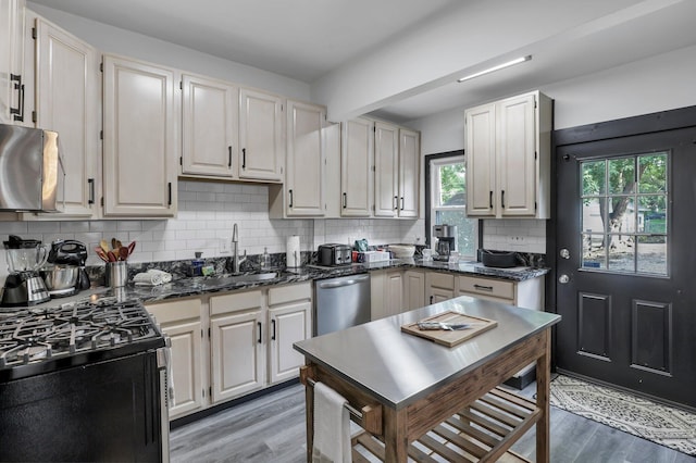kitchen with appliances with stainless steel finishes, tasteful backsplash, light wood-type flooring, a sink, and dark stone countertops