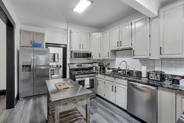kitchen featuring a sink, dark stone counters, stainless steel appliances, and light wood-style flooring
