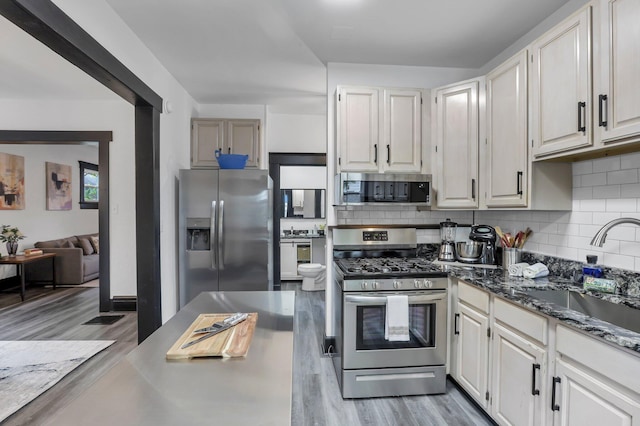 kitchen featuring appliances with stainless steel finishes, decorative backsplash, a sink, and light wood finished floors
