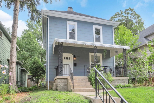 traditional style home with covered porch, a chimney, and a front lawn