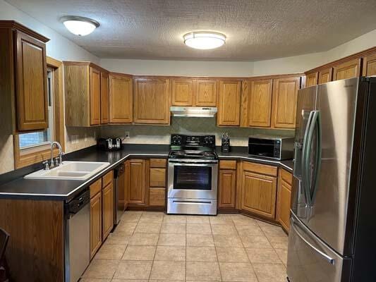 16900 Thompson Ridge Rd, Laurelville, OH 43135 - kitchen with under cabinet range hood, dark countertops, stainless steel appliances, and a sink