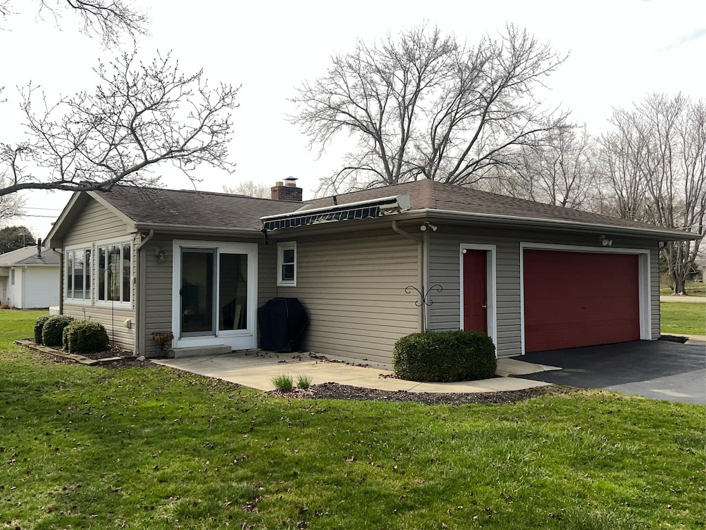 back of property with a lawn, roof with shingles, a chimney, and driveway