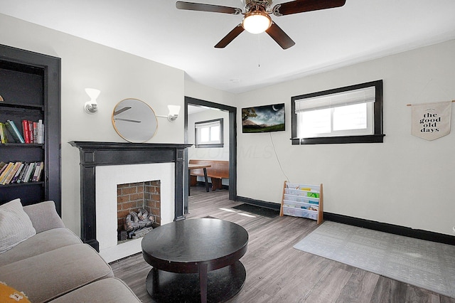 living room featuring baseboards, ceiling fan, a fireplace, and wood finished floors