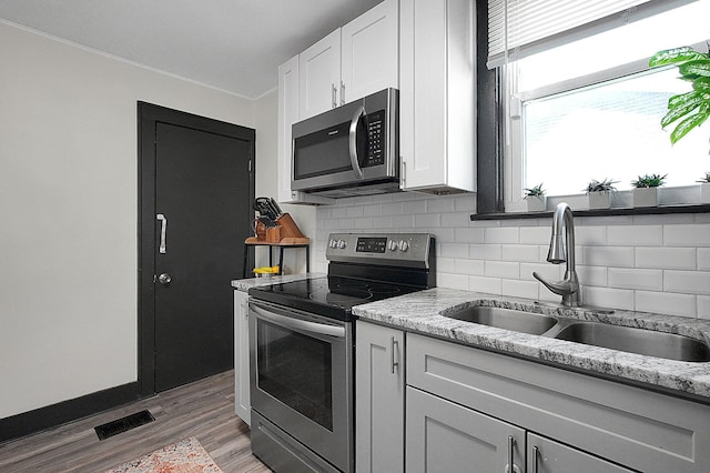 kitchen featuring white cabinets, a sink, light wood finished floors, appliances with stainless steel finishes, and backsplash