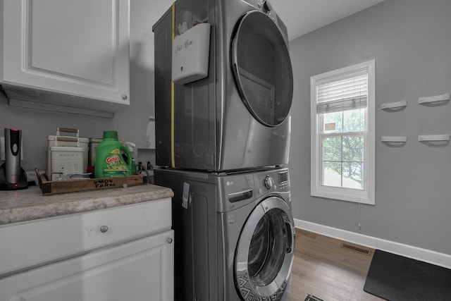 clothes washing area with light wood finished floors, stacked washer / drying machine, cabinet space, visible vents, and baseboards