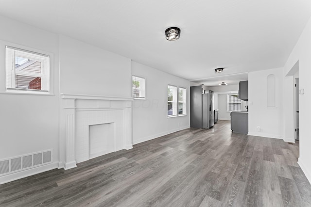 unfurnished living room with a fireplace, baseboards, visible vents, and dark wood finished floors