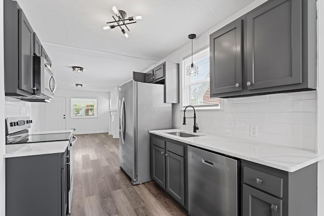 kitchen with gray cabinetry, a sink, decorative backsplash, dark wood-type flooring, and appliances with stainless steel finishes