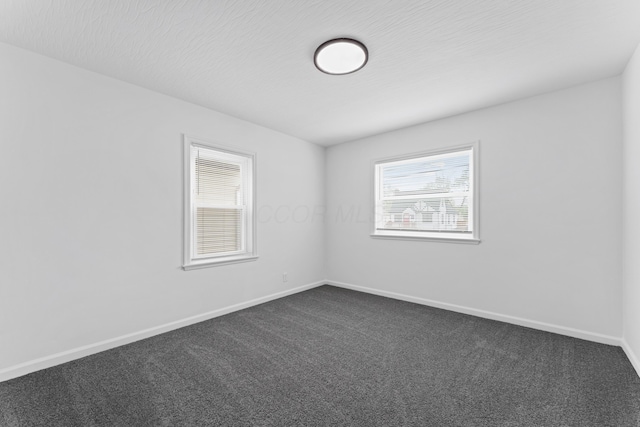 spare room featuring baseboards and dark colored carpet