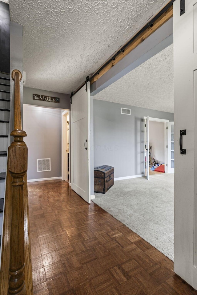 corridor with visible vents, a barn door, baseboards, and a textured ceiling