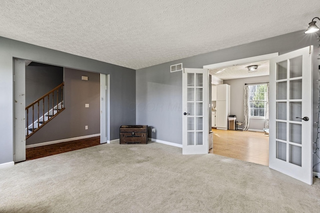 empty room with a textured ceiling, french doors, carpet, baseboards, and stairway