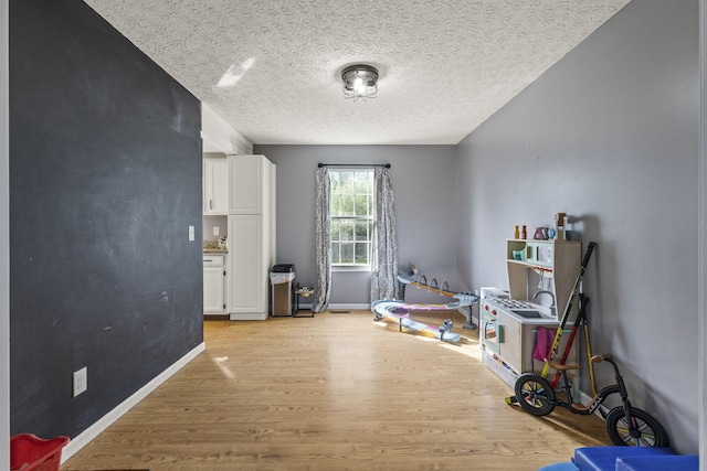interior space with baseboards, light wood finished floors, and a textured ceiling