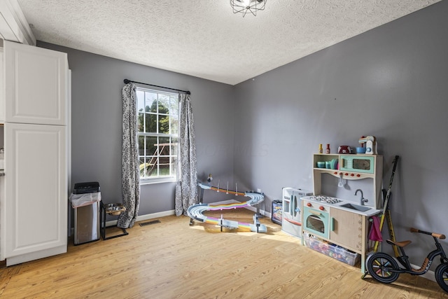 rec room featuring baseboards, light wood-type flooring, a textured ceiling, and visible vents