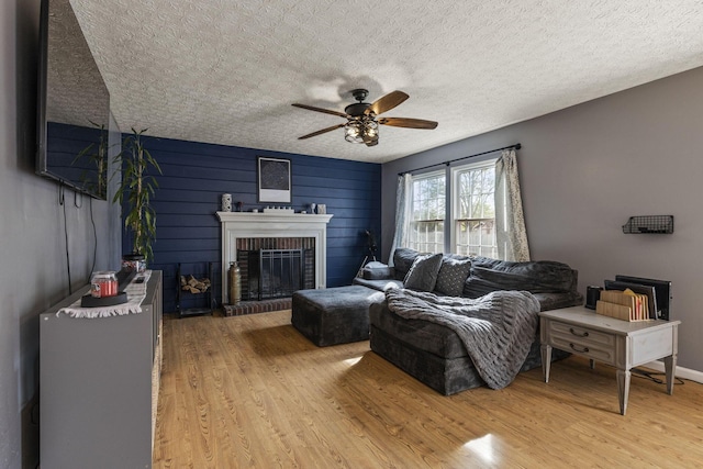 living area featuring a ceiling fan, a brick fireplace, and wood finished floors
