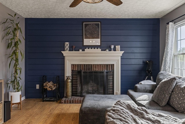 living room featuring ceiling fan, a textured ceiling, a brick fireplace, wood finished floors, and baseboards