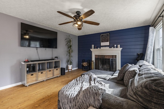 living room with wood finished floors, a fireplace, baseboards, ceiling fan, and a textured ceiling