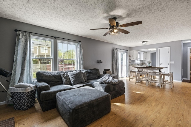 living area featuring baseboards, a textured ceiling, ceiling fan, and light wood-style flooring