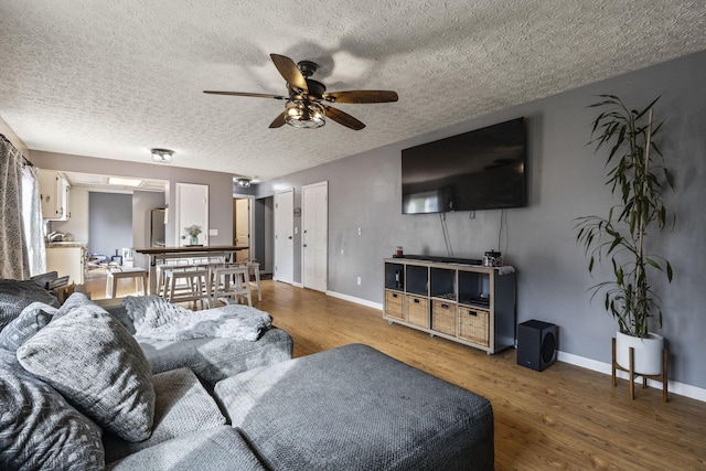 living room featuring baseboards, a textured ceiling, ceiling fan, and wood finished floors