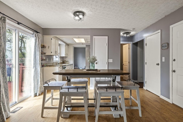 dining room featuring light wood-type flooring, a textured ceiling, and visible vents