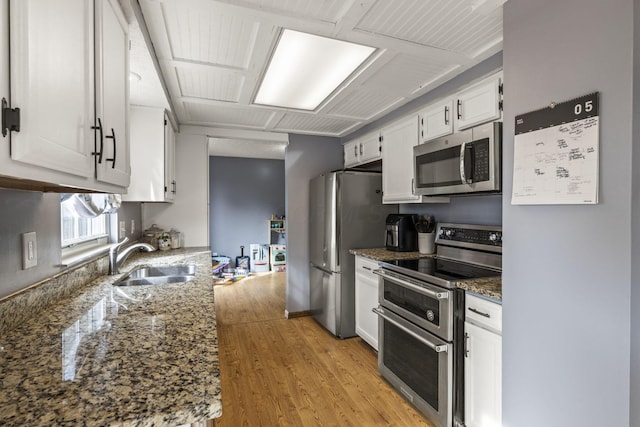 kitchen featuring dark stone countertops, white cabinetry, a sink, light wood finished floors, and appliances with stainless steel finishes
