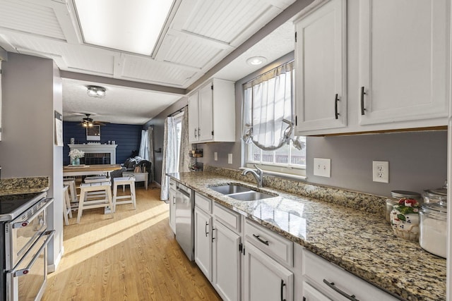 kitchen with stainless steel dishwasher, a sink, white cabinets, and light wood-type flooring