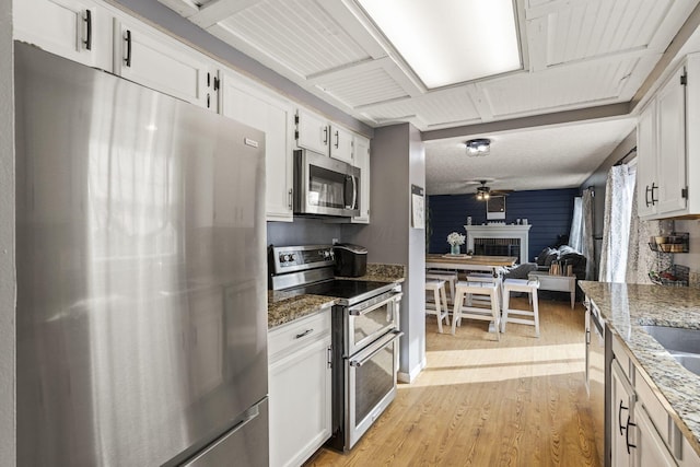 kitchen featuring stainless steel appliances, white cabinetry, light wood finished floors, and a fireplace
