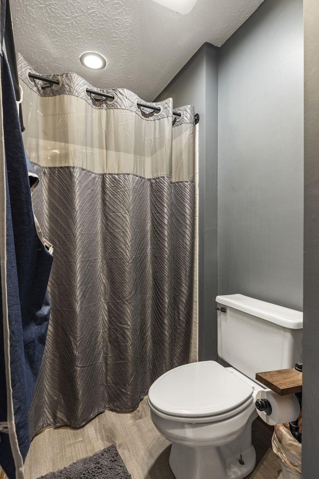 bathroom with a shower with shower curtain, toilet, a textured ceiling, and wood finished floors