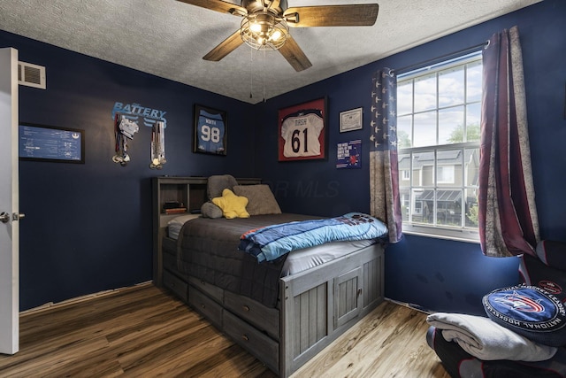 bedroom featuring a textured ceiling, multiple windows, wood finished floors, and visible vents