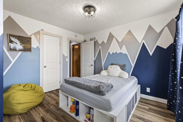bedroom featuring a textured ceiling, baseboards, wood finished floors, and visible vents