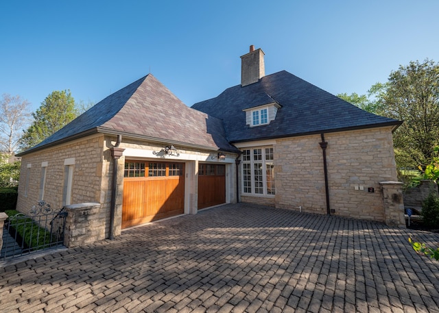 2528 Onandaga Dr, Upper Arlington, OH 43221 - rear view of house featuring stone siding, a chimney, an attached garage, decorative driveway, and a high end roof