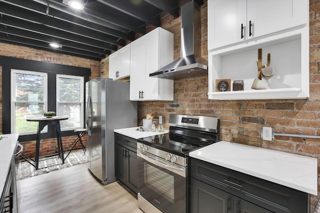 1010 Bruck St, Columbus, OH 43206 - kitchen featuring brick wall, wall chimney exhaust hood, white cabinets, light wood finished floors, and appliances with stainless steel finishes