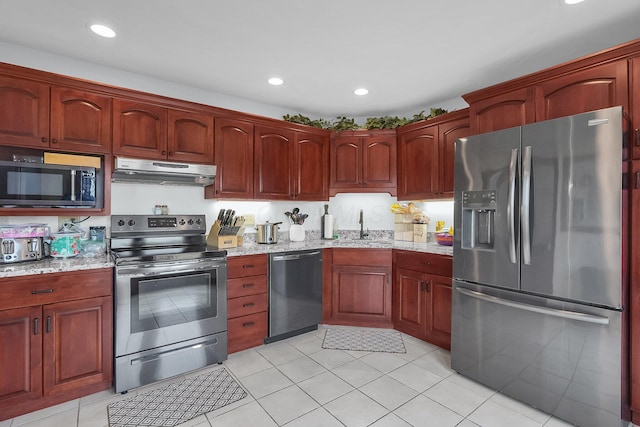 kitchen with under cabinet range hood, stainless steel appliances, a sink, and light stone counters
