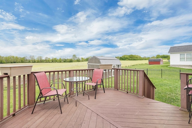 wooden terrace featuring a rural view, a lawn, a fenced backyard, a shed, and an outbuilding