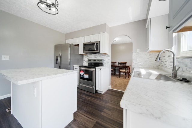 kitchen featuring arched walkways, tasteful backsplash, a sink, white cabinets, and stainless steel appliances