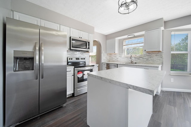 kitchen with a sink, arched walkways, dark wood finished floors, stainless steel appliances, and tasteful backsplash