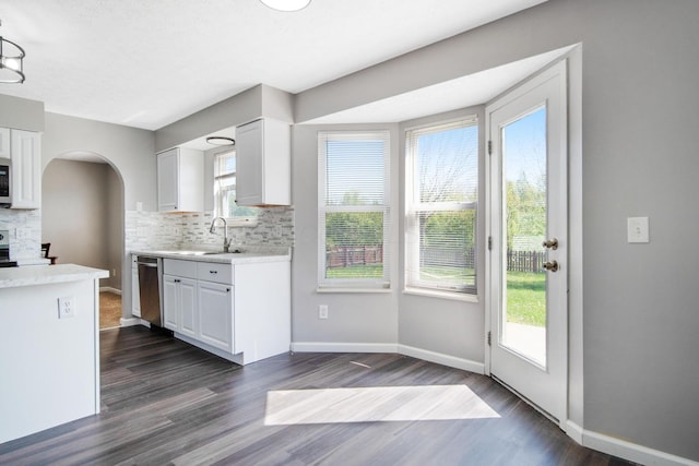 kitchen featuring arched walkways, dark wood finished floors, a sink, light countertops, and stainless steel appliances