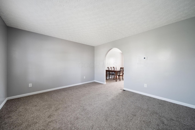 carpeted spare room featuring baseboards, arched walkways, and a textured ceiling