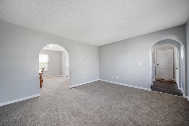 unfurnished room featuring carpet flooring, arched walkways, baseboards, and a textured ceiling