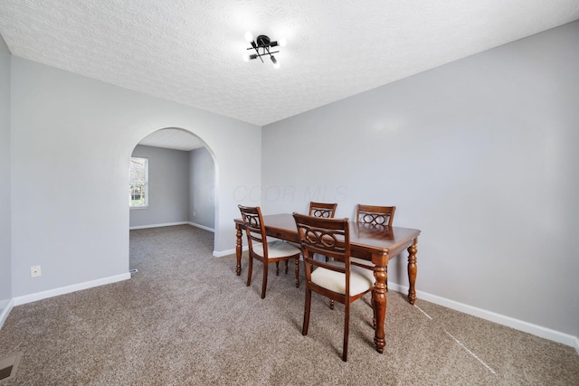 dining area featuring baseboards, arched walkways, a textured ceiling, and light carpet