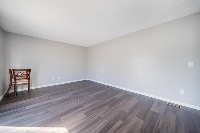 unfurnished room with baseboards, a textured ceiling, dark wood-style flooring, and visible vents