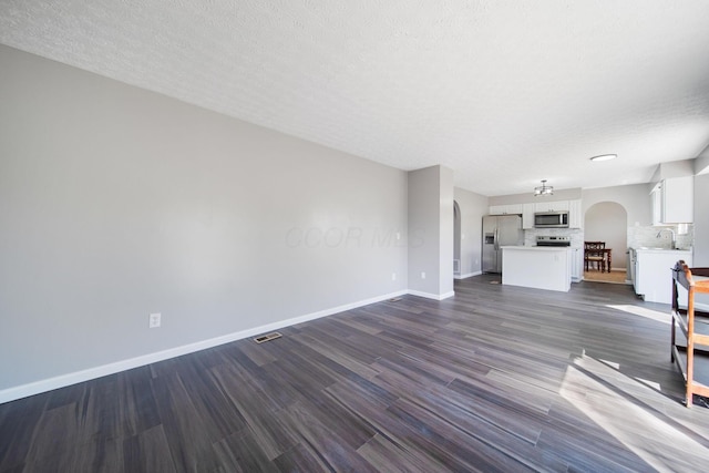 unfurnished living room with arched walkways, baseboards, dark wood-style floors, and a sink