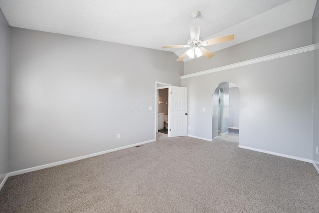 carpeted empty room with vaulted ceiling, arched walkways, baseboards, and a ceiling fan