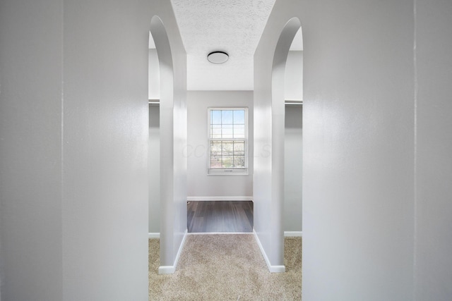 hallway with arched walkways, baseboards, carpet, and a textured ceiling